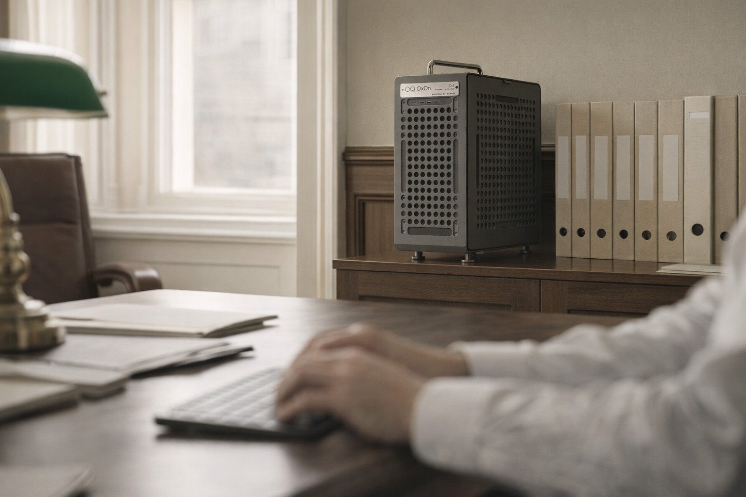 A solicitor&rsquo;s office: hands on a keyboard out of focus, a green desk lamp, and the Ox1 on a cabinet among lever-arch files.